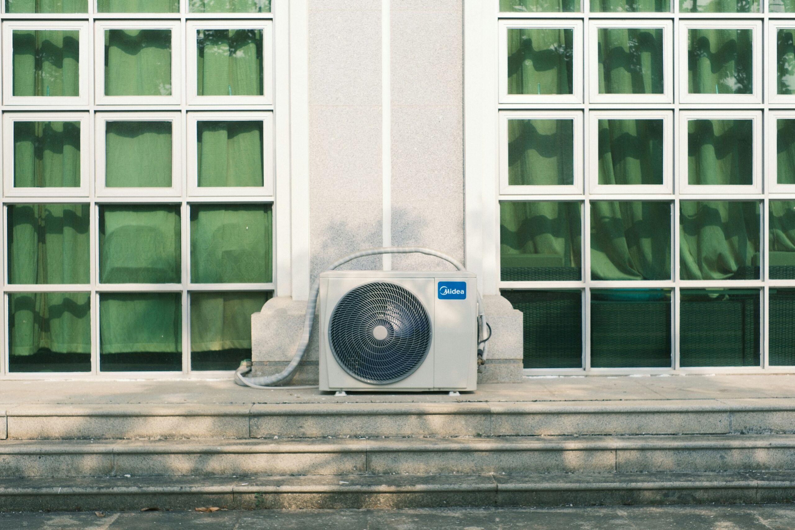 Outdoor air-conditioning unit below large windows on a sunny day