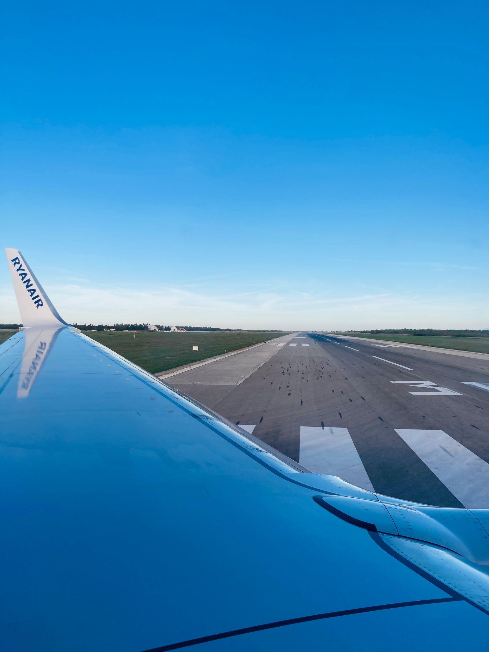 View from an airplane window showing a wing over a runway before takeoff