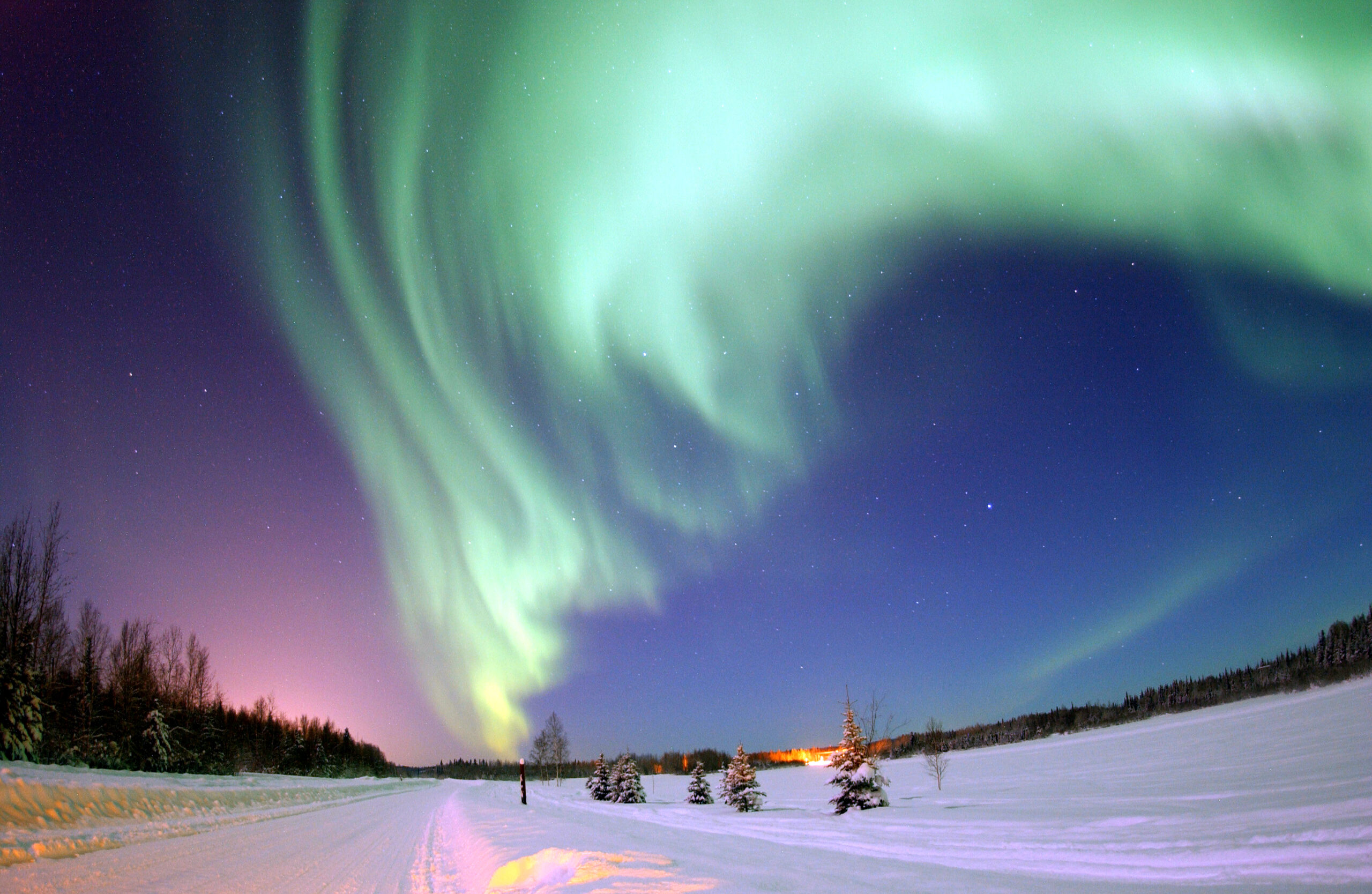 Bright green aurora above a dark lake, a visible sign of charged particles interacting with the upper atmosphere