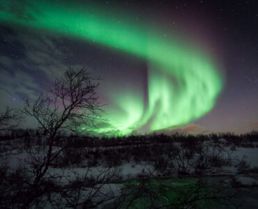 Green aurora borealis curtains glowing over a snowy night landscape in Norway