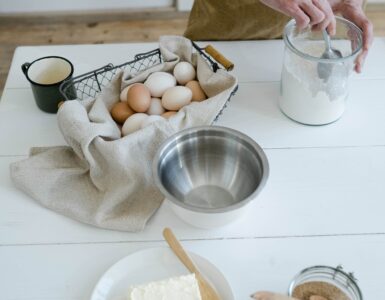 Baking ingredients arranged on a white table with flour, eggs, butter, and a mixing bowl
