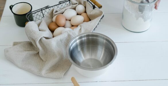 Baking ingredients arranged on a white table with flour, eggs, butter, and a mixing bowl