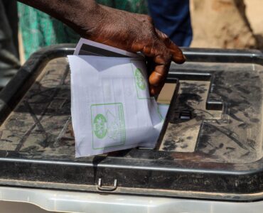 A voter places a paper ballot into a ballot box