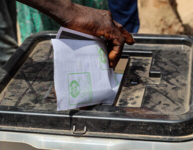 A voter places a paper ballot into a ballot box