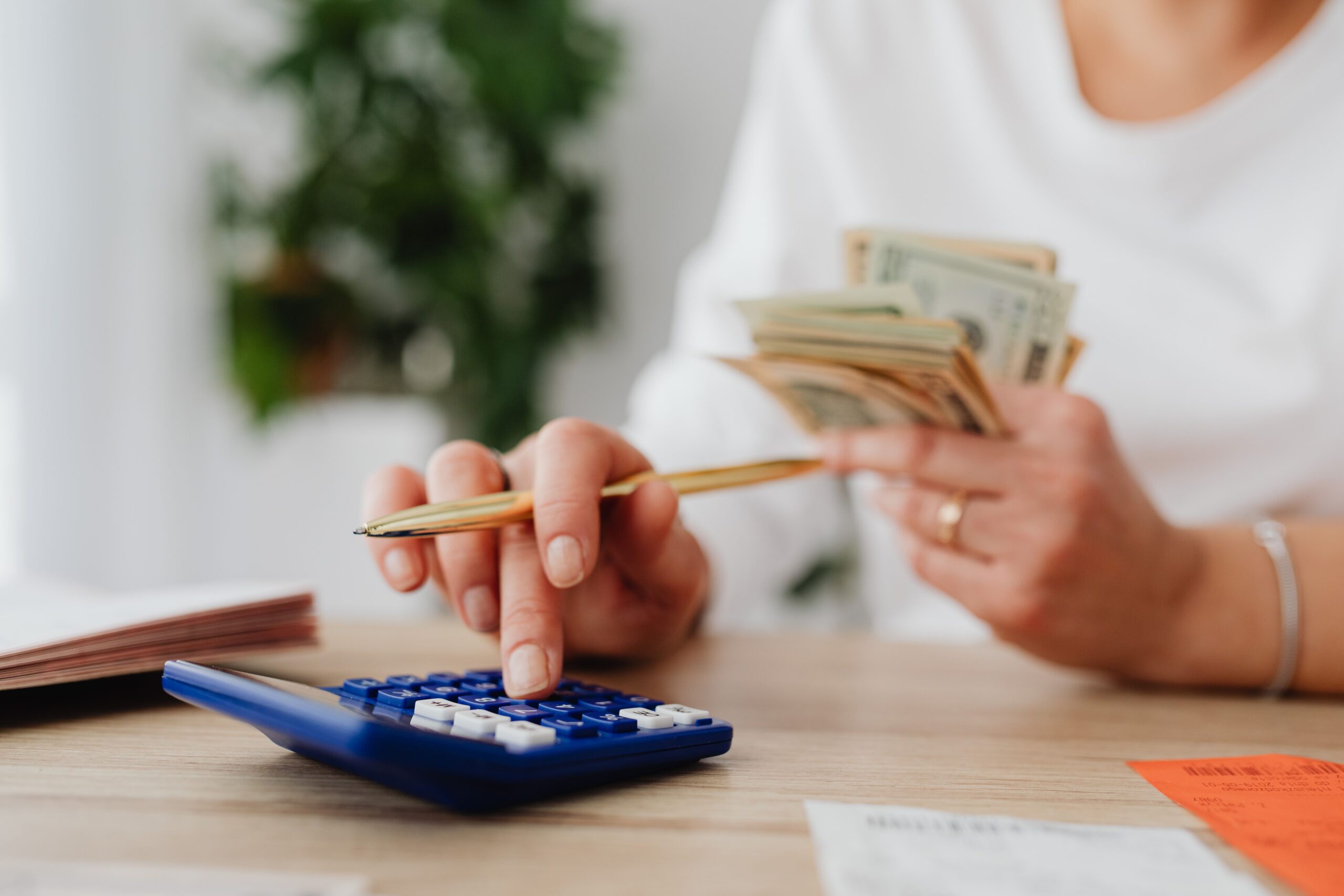 A person uses a calculator while counting cash and reviewing finances.