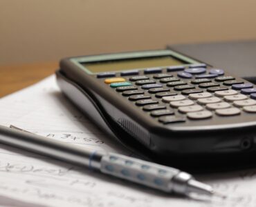 A calculator and pen on handwritten calculus notes for practicing related rates and derivatives.
