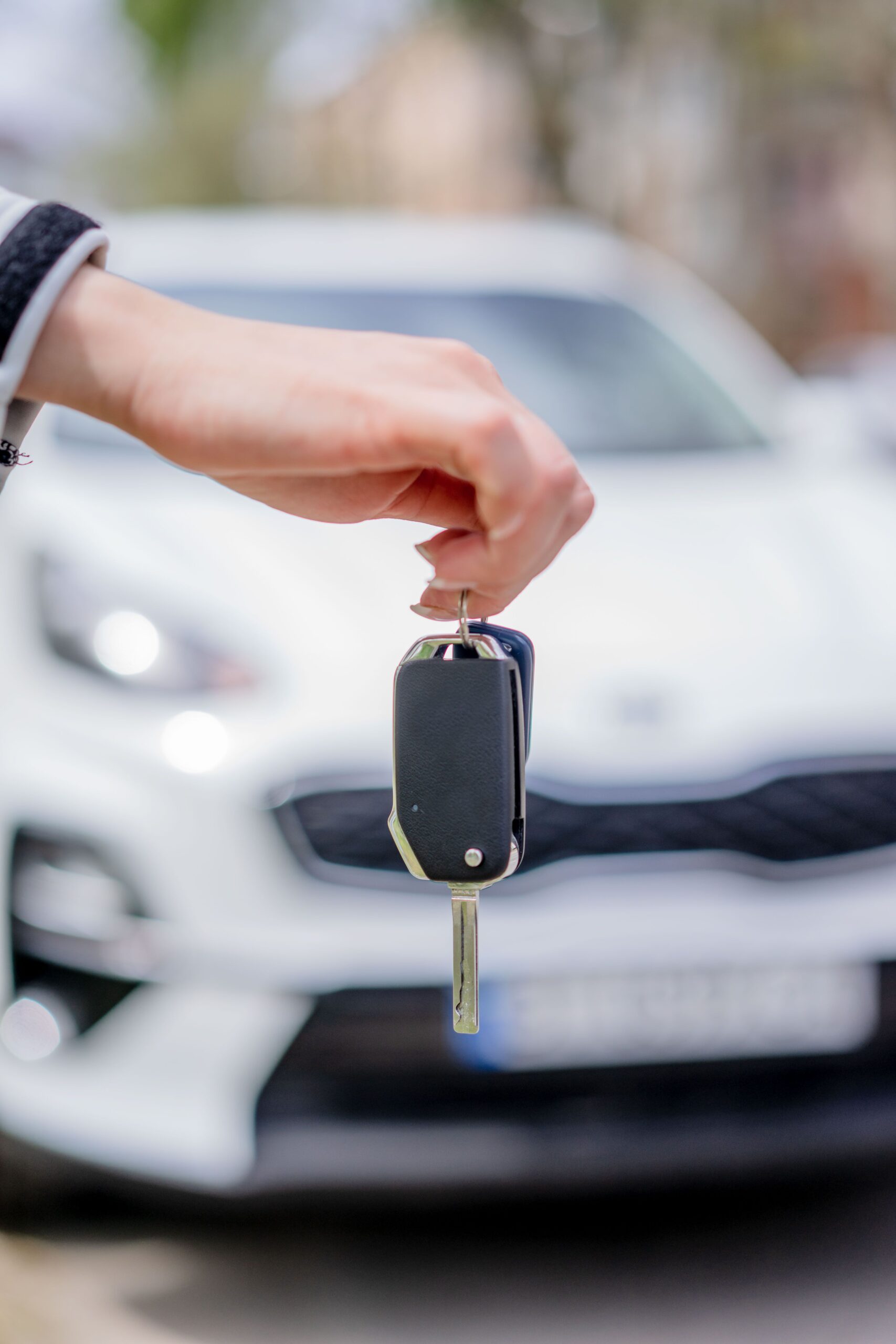 A hand holds a car key in front of a parked vehicle