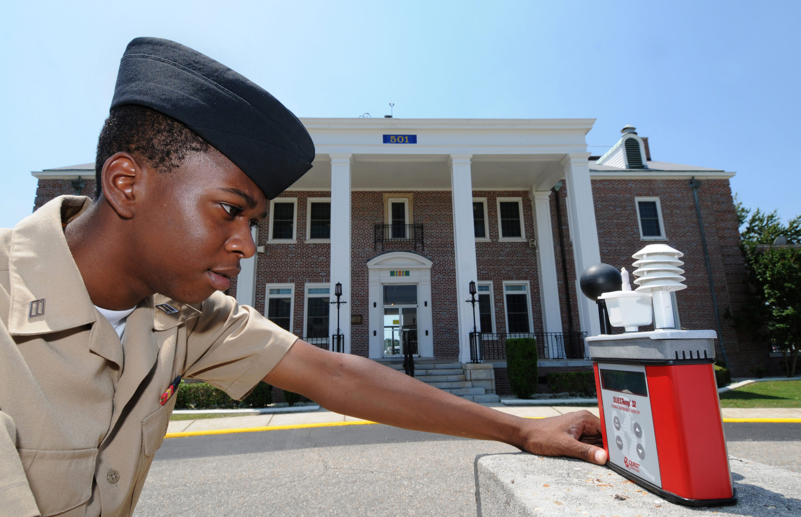 A person checks a wet bulb globe temperature meter outdoors during hot conditions.