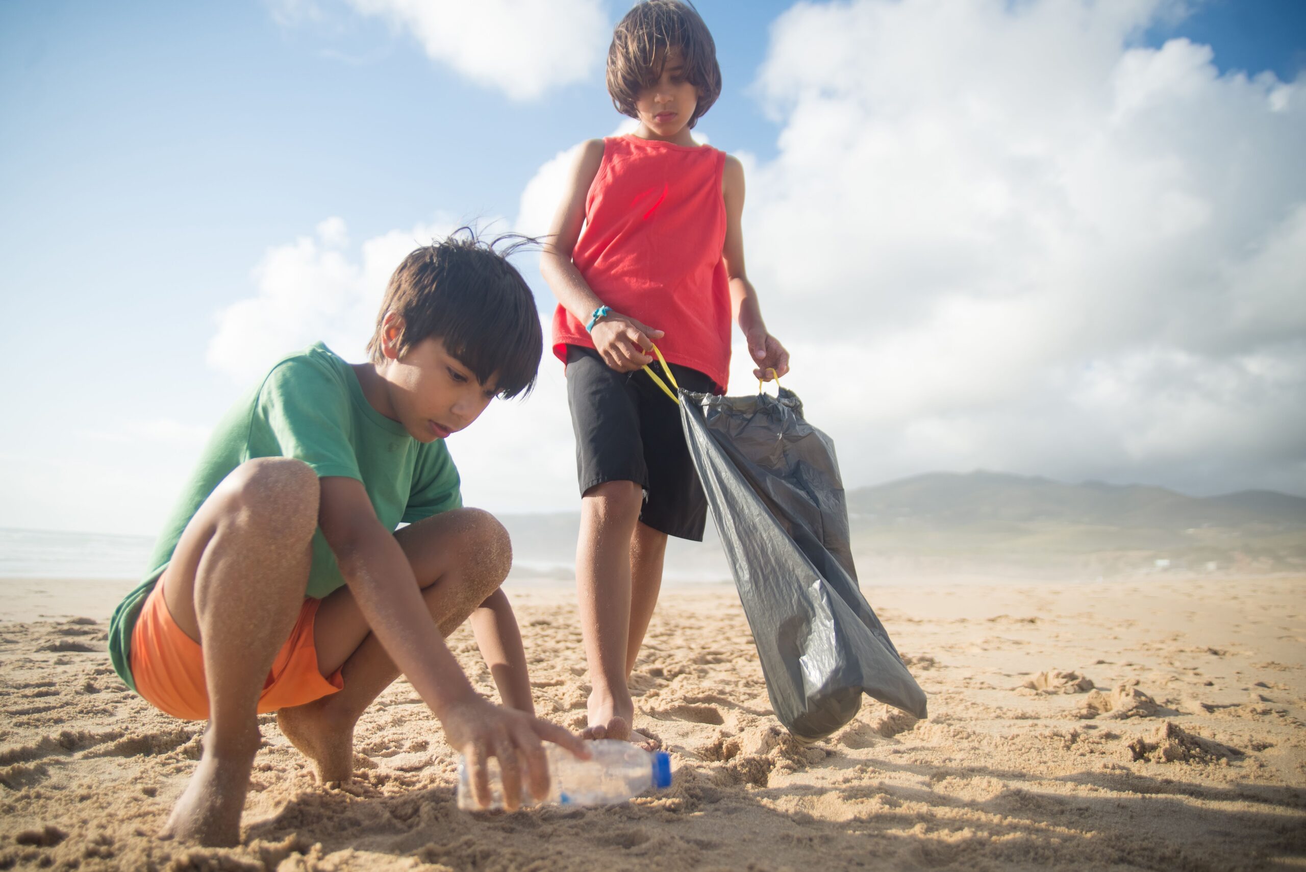 Children picking up a plastic bottle during a beach cleanup
