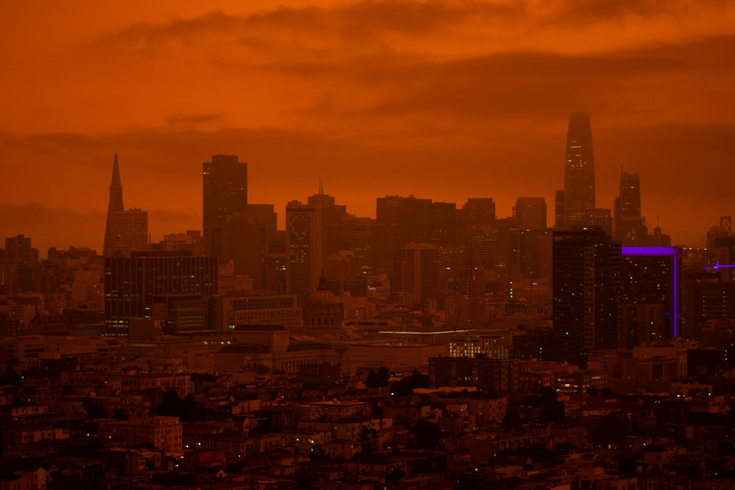 A city skyline under orange wildfire smoke haze