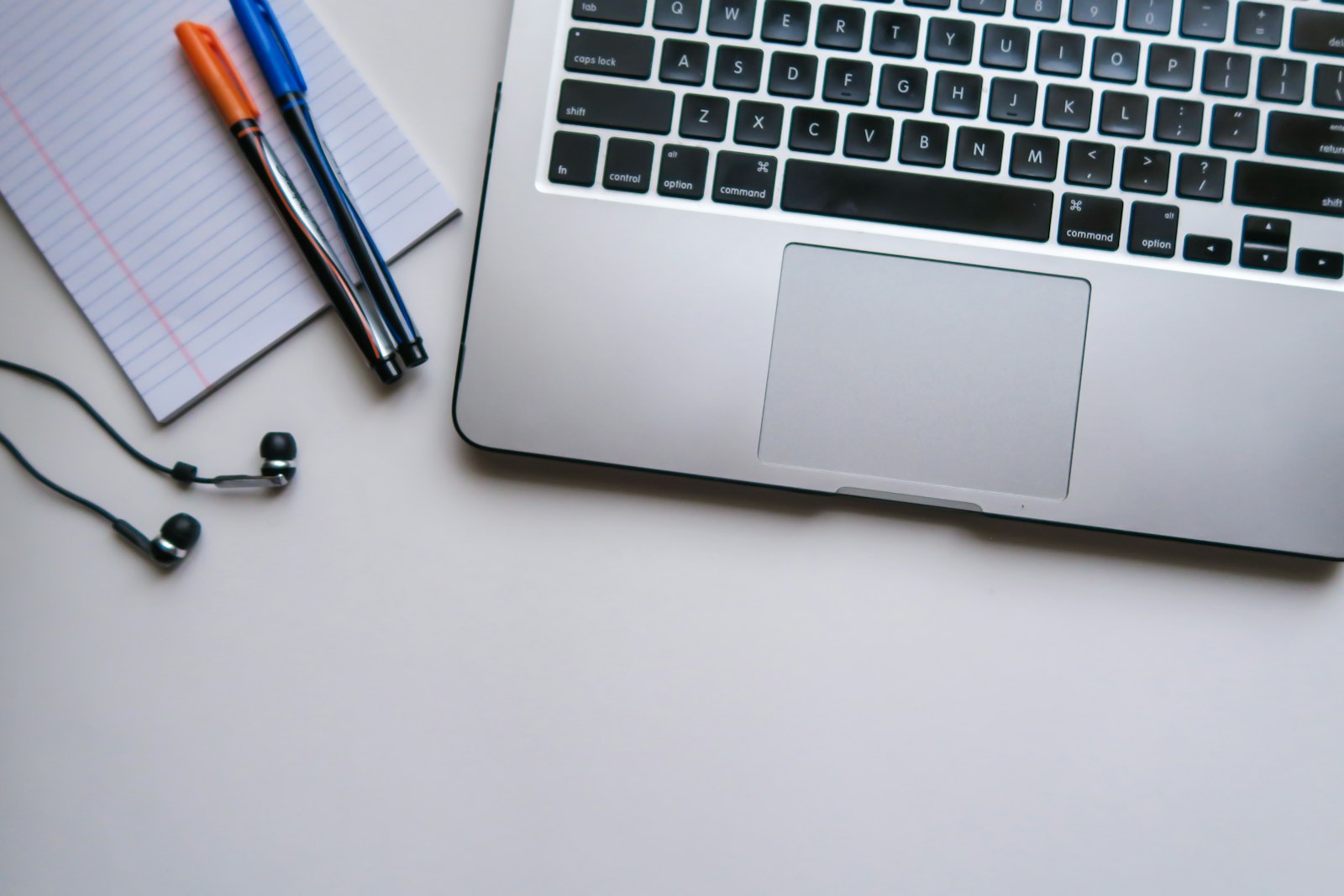 A laptop, notebook, pens, and earbuds arranged for exam preparation.
