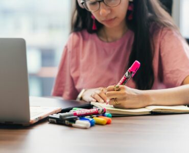 A student writes notes beside a laptop while planning a college personal statement.
