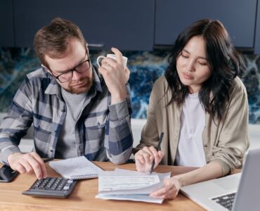 Two people review household bills with a calculator and laptop.