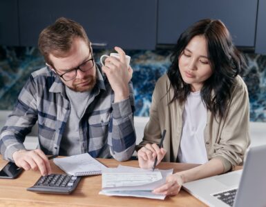 Two people review household bills with a calculator and laptop.