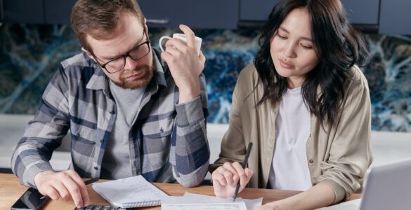 Two people review household bills with a calculator and laptop.