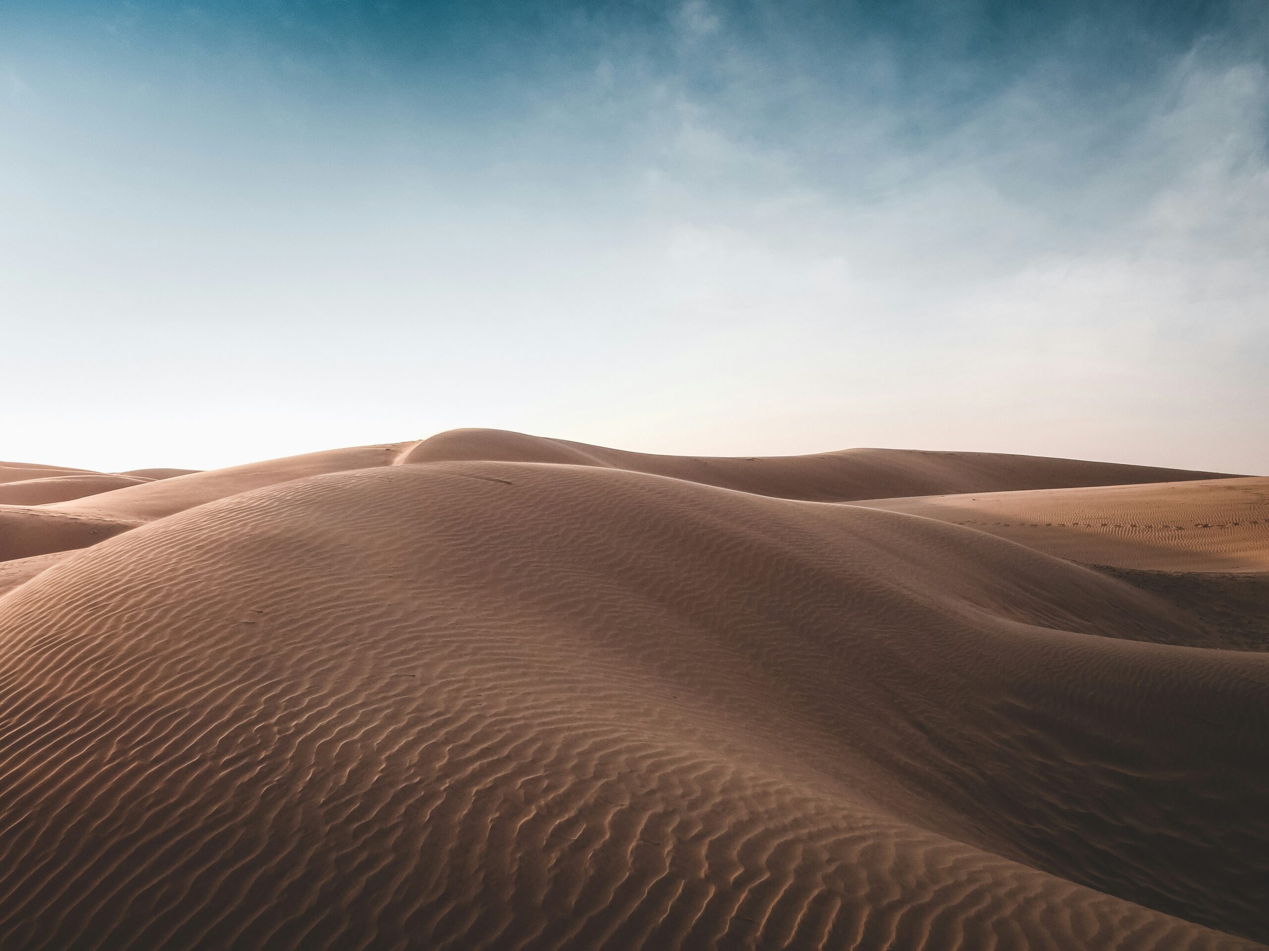 Wind-shaped desert sand dunes beneath a pale blue sky
