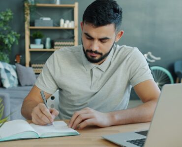A notebook and laptop on a desk while a student drafts supplemental college essays.