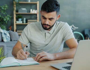 A notebook and laptop on a desk while a student drafts supplemental college essays.