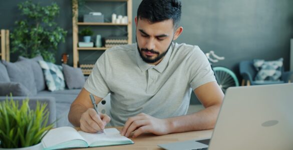 A notebook and laptop on a desk while a student drafts supplemental college essays.
