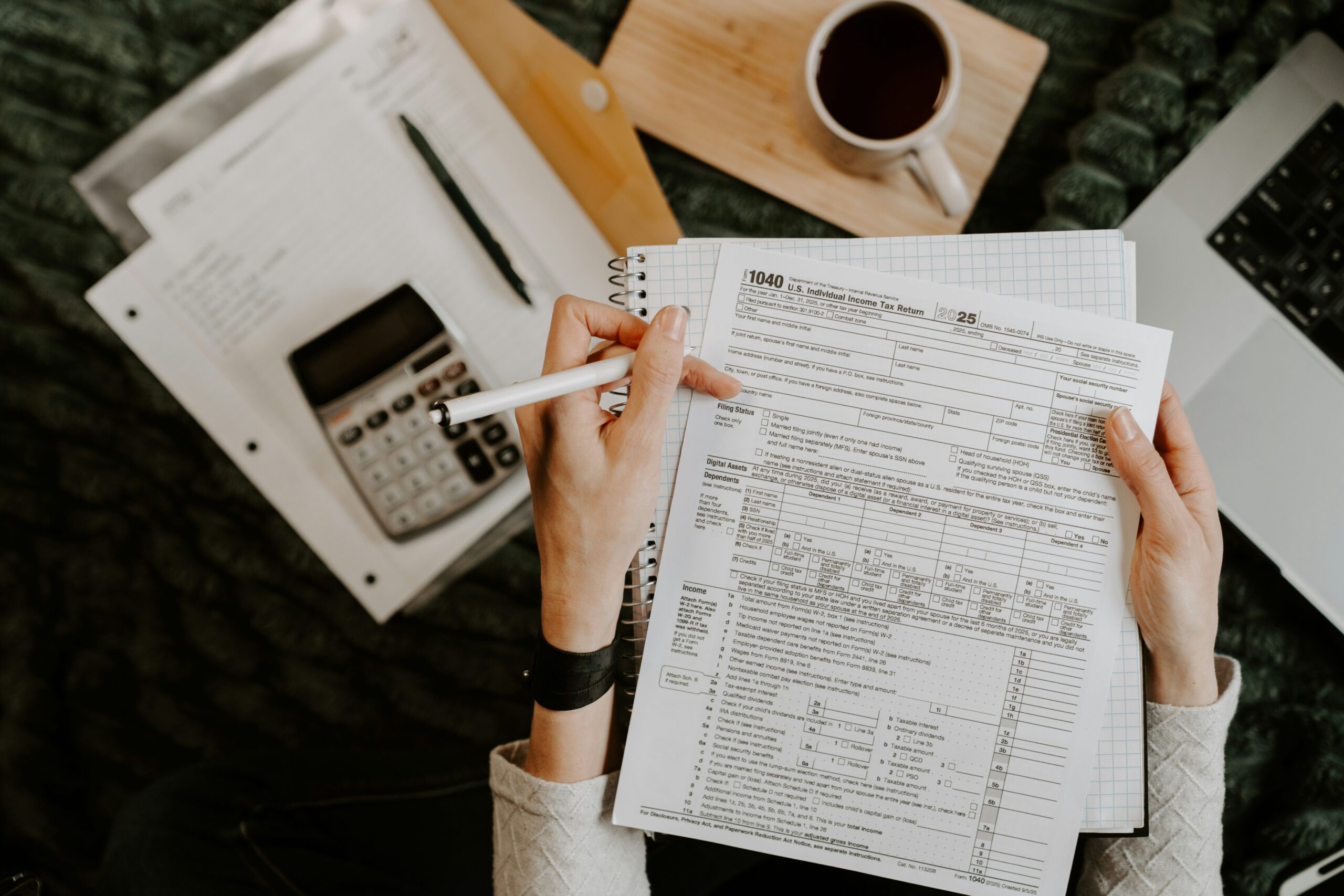 Financial forms, a notebook, and a calculator arranged beside a laptop.