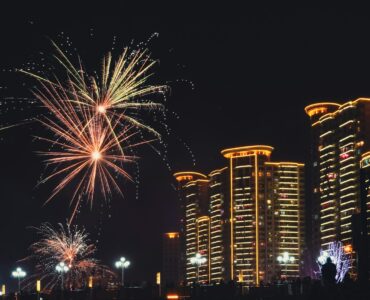Fireworks bursting over a city skyline with smoke drifting through the night sky