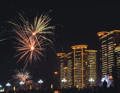 Fireworks bursting over a city skyline with smoke drifting through the night sky
