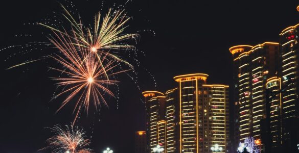 Fireworks bursting over a city skyline with smoke drifting through the night sky