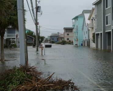 A coastal neighborhood street filled with floodwater near homes and utility poles