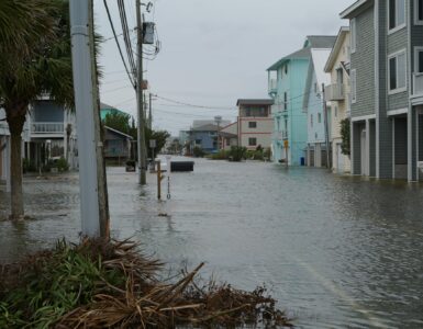 A coastal neighborhood street filled with floodwater near homes and utility poles