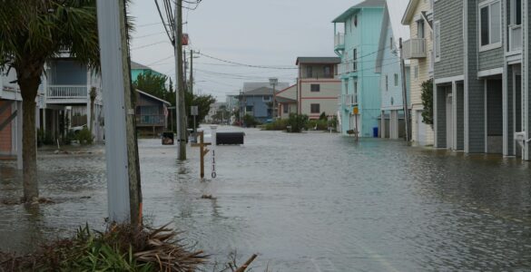 A coastal neighborhood street filled with floodwater near homes and utility poles