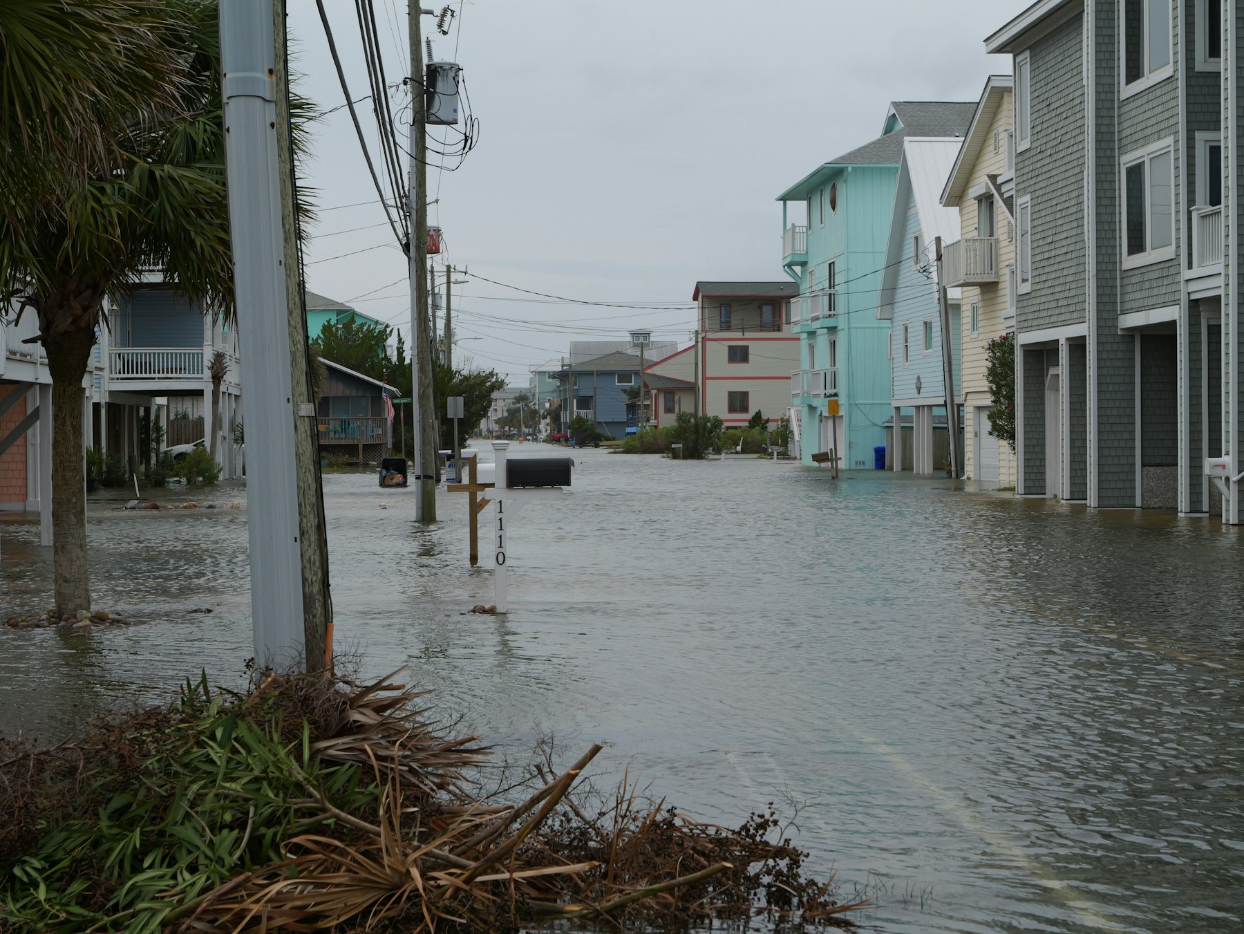 A coastal neighborhood street filled with floodwater near homes and utility poles
