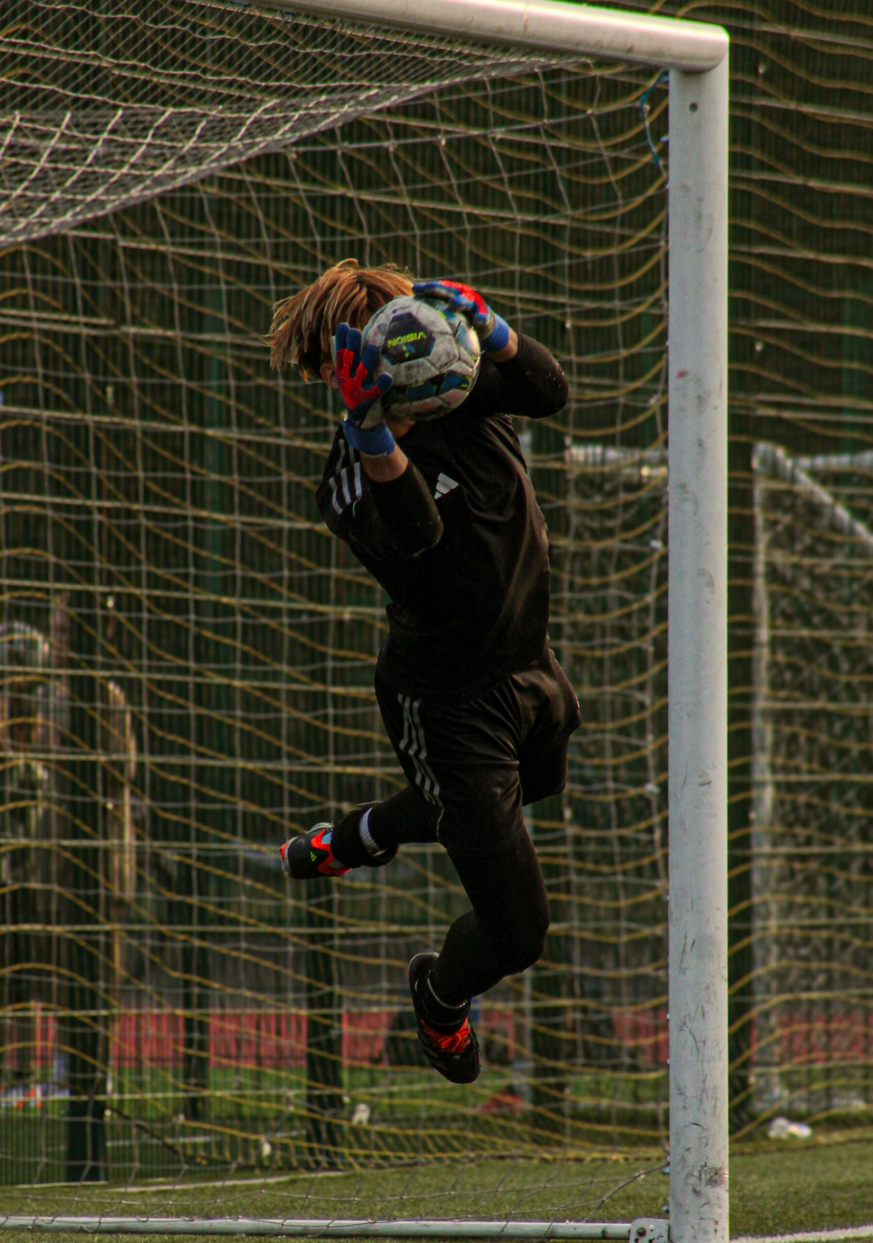 A goalkeeper catches a soccer ball in front of the goal.