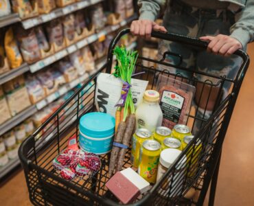 A shopper pushing a grocery cart filled with food in a supermarket aisle