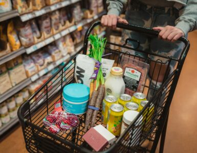 A shopper pushing a grocery cart filled with food in a supermarket aisle