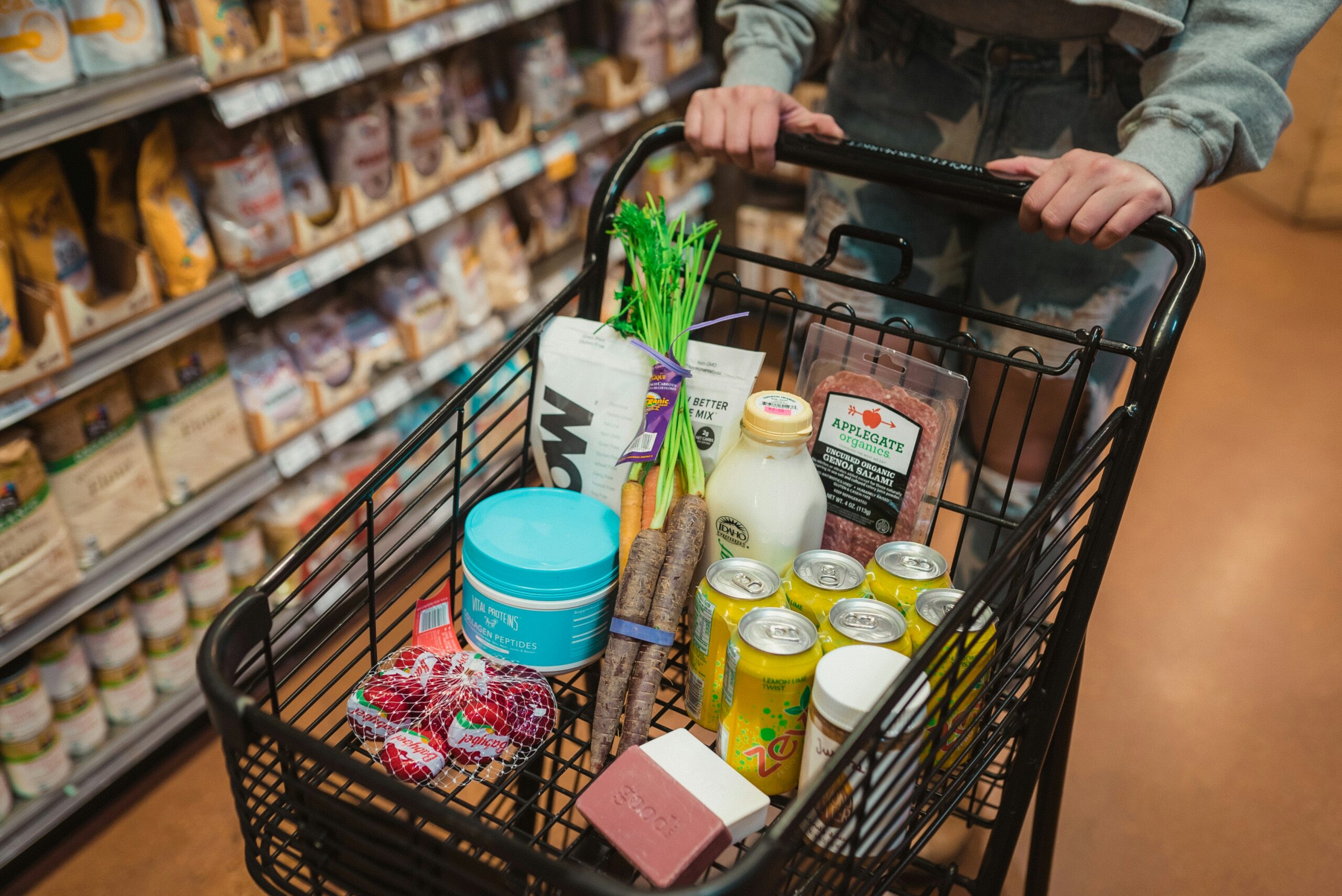 A shopper pushing a grocery cart filled with food in a supermarket aisle.