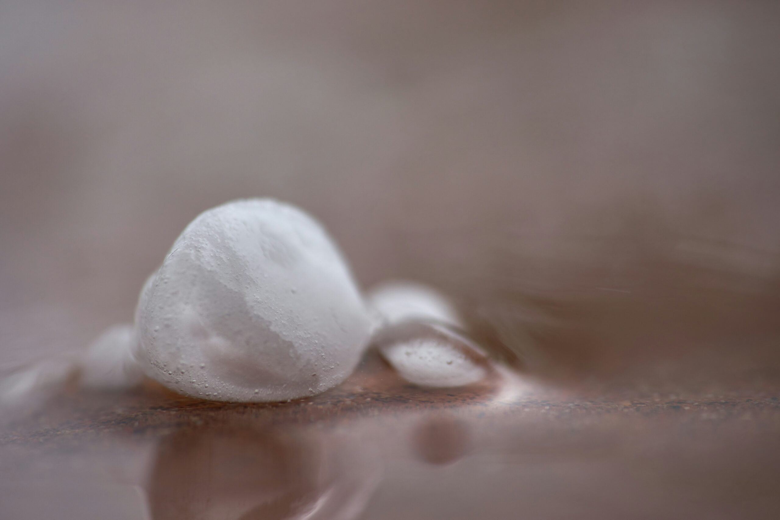 Close-up of white hailstones beginning to melt on a wooden surface.