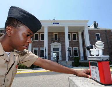 A person checks a wet bulb globe temperature meter during hot outdoor conditions.