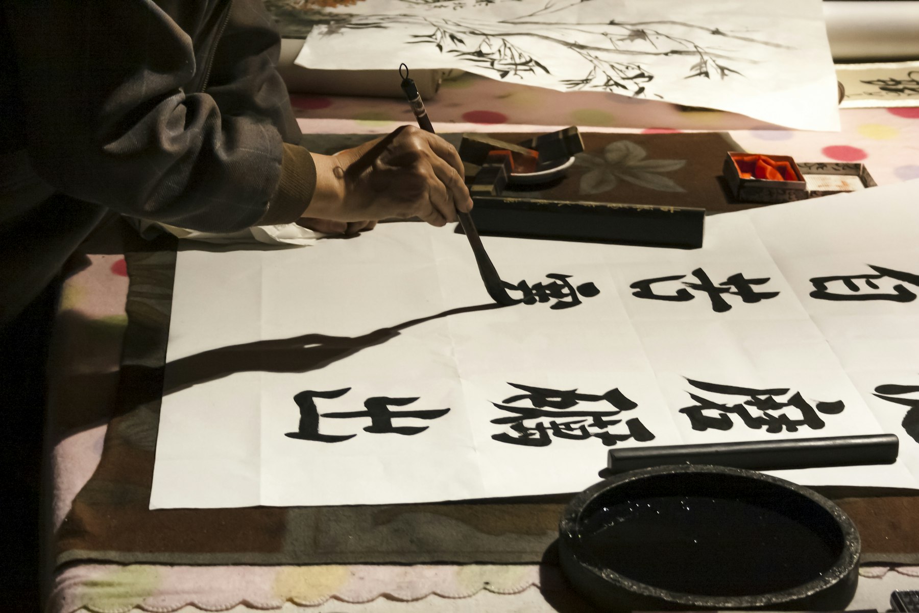 A person practices Japanese writing with brush and ink on white paper.