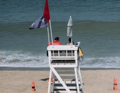 A lifeguard tower with beach flags on a sandy beach near the ocean.