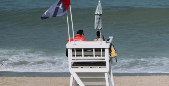 A lifeguard tower with beach flags on a sandy beach near the ocean.