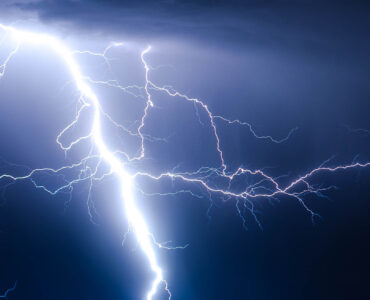 A bright lightning strike branching from dark storm clouds toward the ground