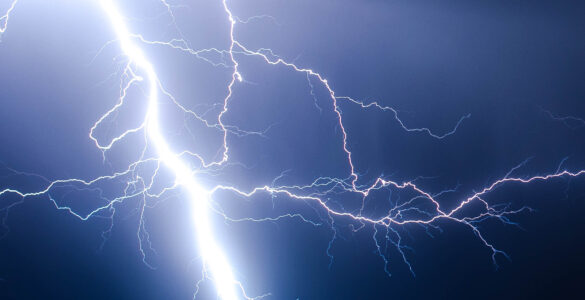 A bright lightning strike branching from dark storm clouds toward the ground