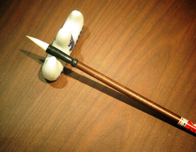A Chinese calligraphy brush beside paper, suggesting careful attention to Mandarin characters and sentence endings.