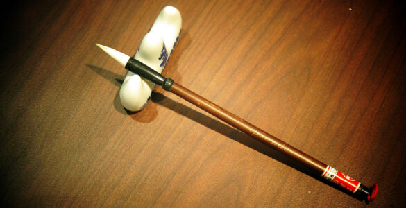 A Chinese calligraphy brush beside paper, suggesting careful attention to Mandarin characters and sentence endings.