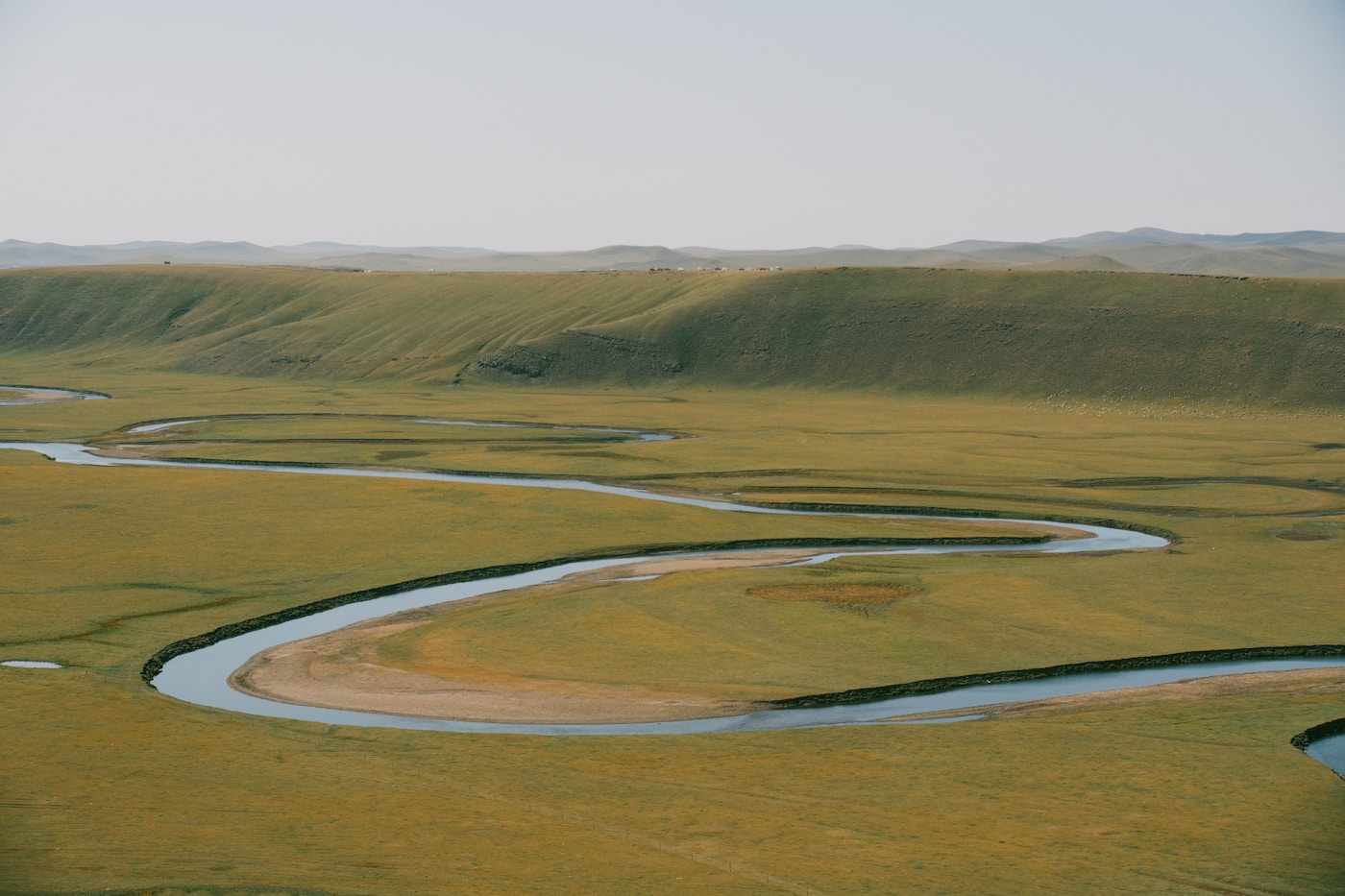 A winding river moving through a broad grassy floodplain