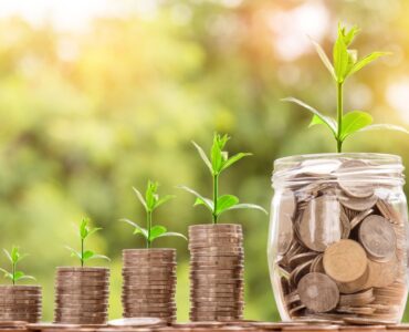 Coin stacks and a jar with small plants growing from them, symbolizing savings growth over time
