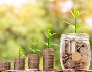 Coin stacks and a jar with small plants growing from them, symbolizing savings growth over time