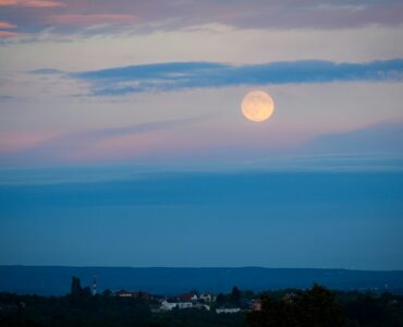 A full moon above a distant landscape at dusk