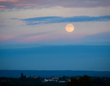 A full moon above a distant landscape at dusk
