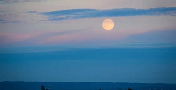 A full moon above a distant landscape at dusk